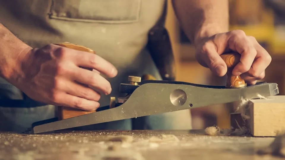 Two hands pushing a hand plane along a length of timber on a workbench
