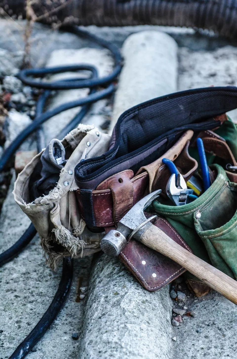 A worn leather tool belt with a hammer and pliers in its pouches, lying on a concrete step